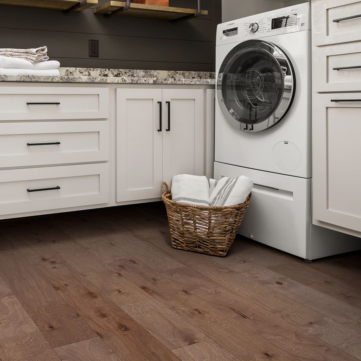 A white laundry basket next to a white washing machine on a brown hardwood floor from Sams Floor Covering in Winchester, KY